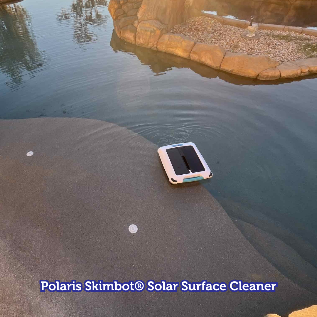 Polaris Skimbot solar surface cleaner on water, near a rocky shore and water edge.