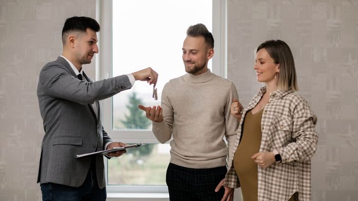 A man is giving a key to a pregnant woman and a man.