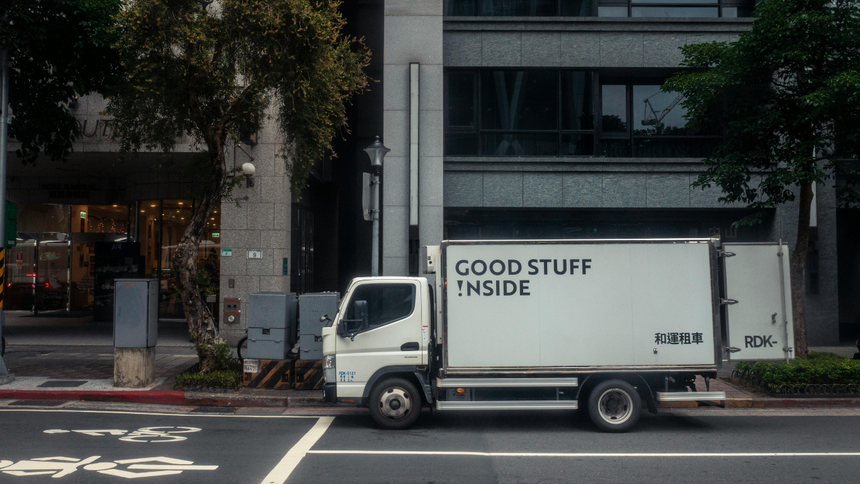 White delivery truck parked on a city street, labeled “GOOD STUFF INSIDE,” in front of a building.