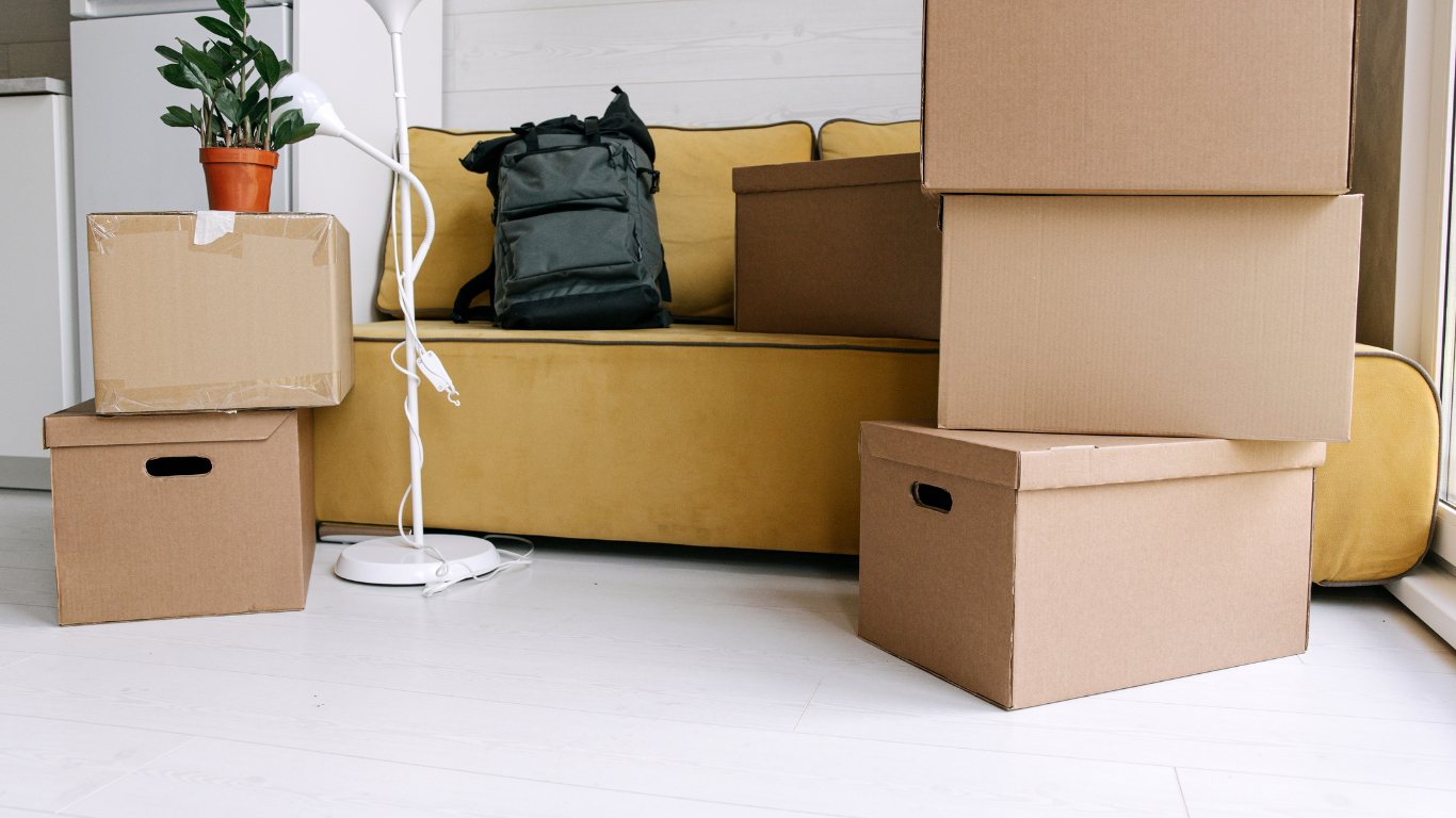 Packed moving boxes and a backpack on a couch in a bright room