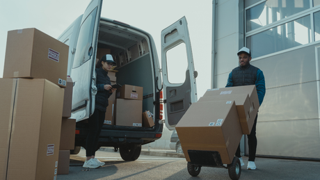 Delivery workers unloading boxes from a white van at a warehouse loading dock