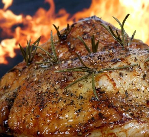 Close-up of a roasted, herb-crusted chicken with rosemary, sizzling against a fiery background