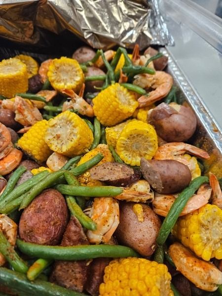Tray of shrimp and sliced corn with green beans and small potatoes on foil