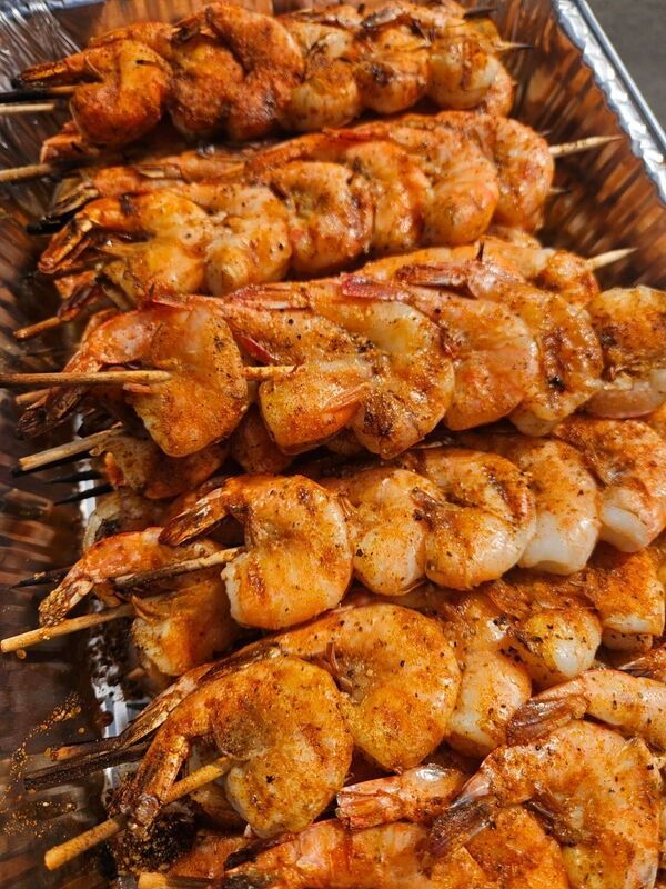 Rows of skewered grilled shrimp coated in orange seasoning on a metal tray
