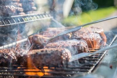 Meat grilling on a barbecue, with smoke rising and tongs turning the food over hot coals