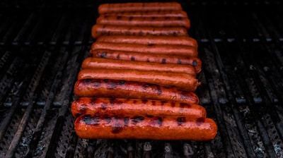 Grilled hot dogs lined up on a barbecue grill, browned with char marks.