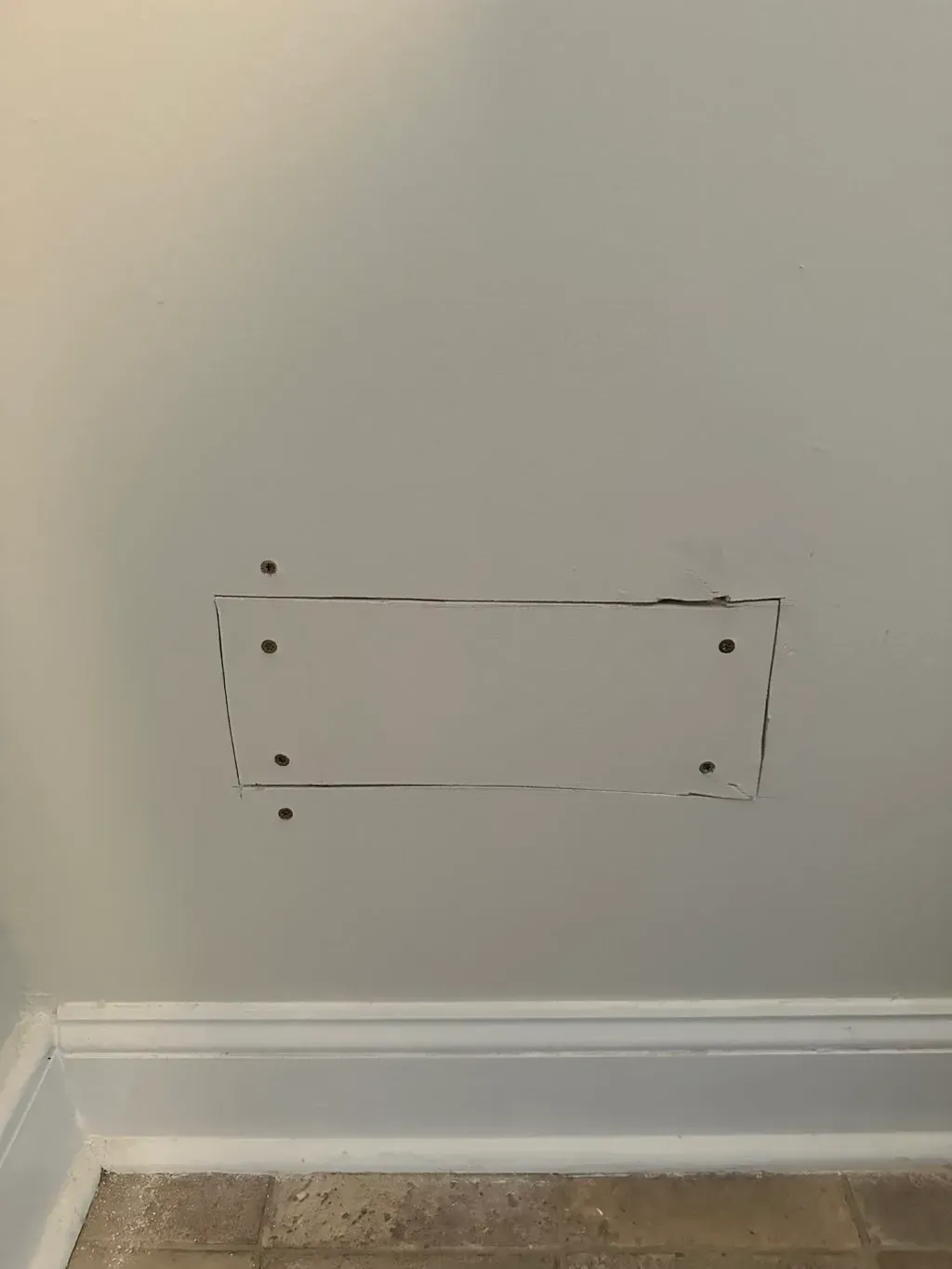 Empty wall above baseboard with a small rectangular outline and screw holes.
