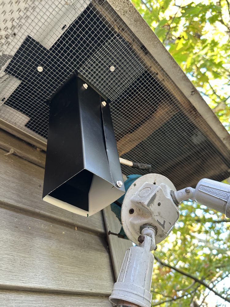 Black outdoor speaker mounted under a roof eave beside a white security camera and wood siding