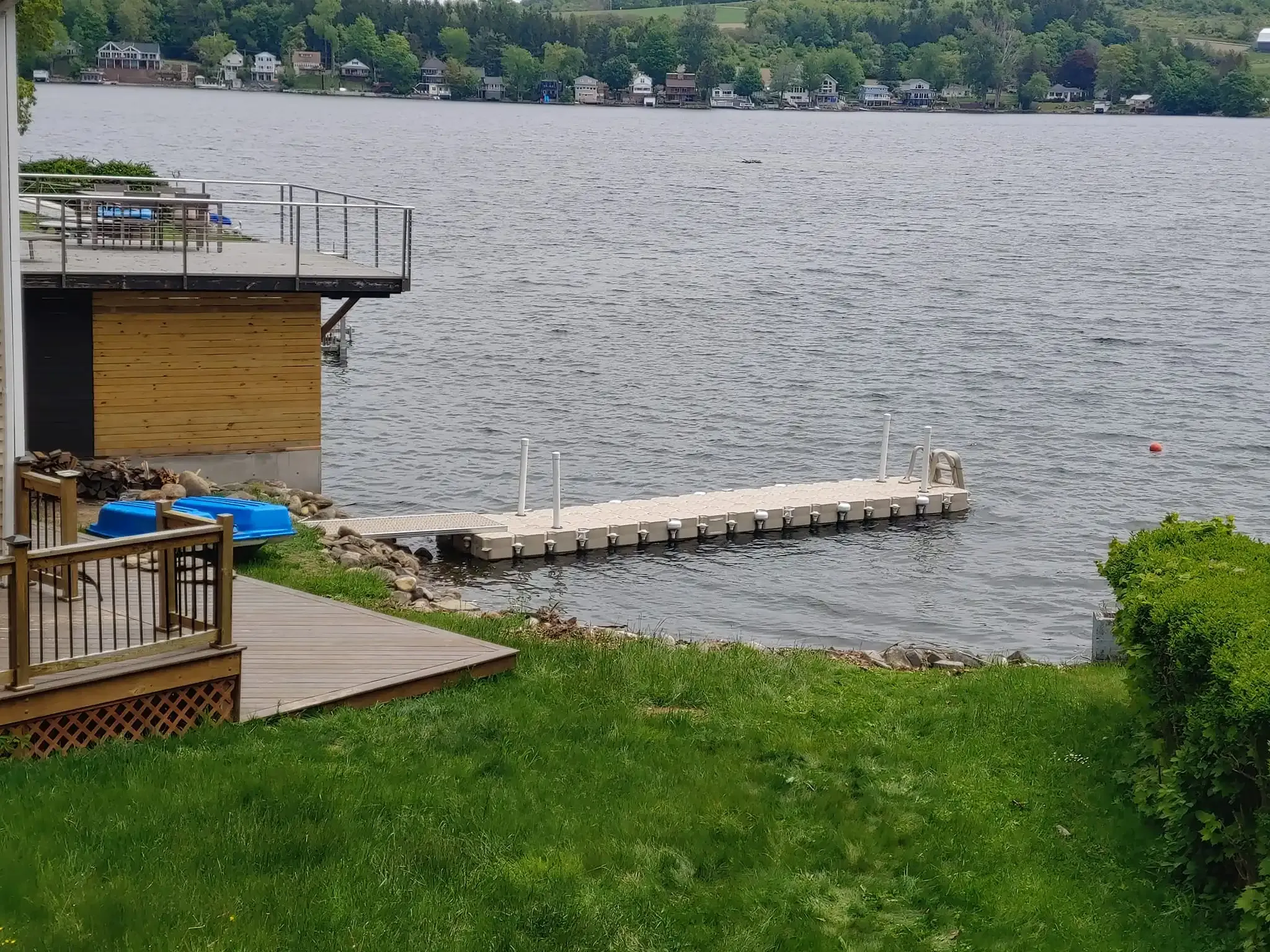 Lakeside dock beside a grassy yard, with rippling water and trees across the shore.