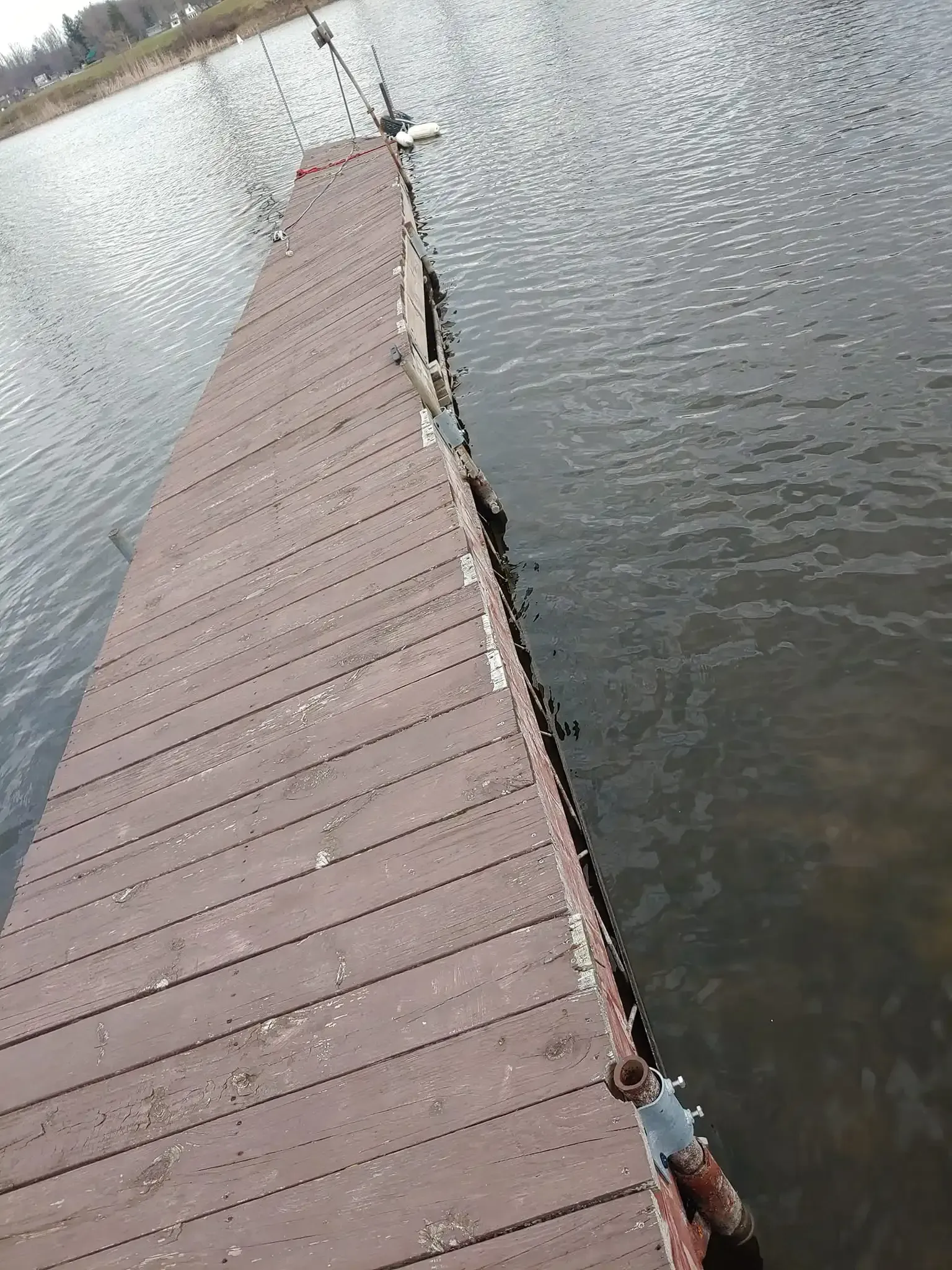 Wooden dock extending into calm water, with ducks at the far end and a rusted edge along the right side