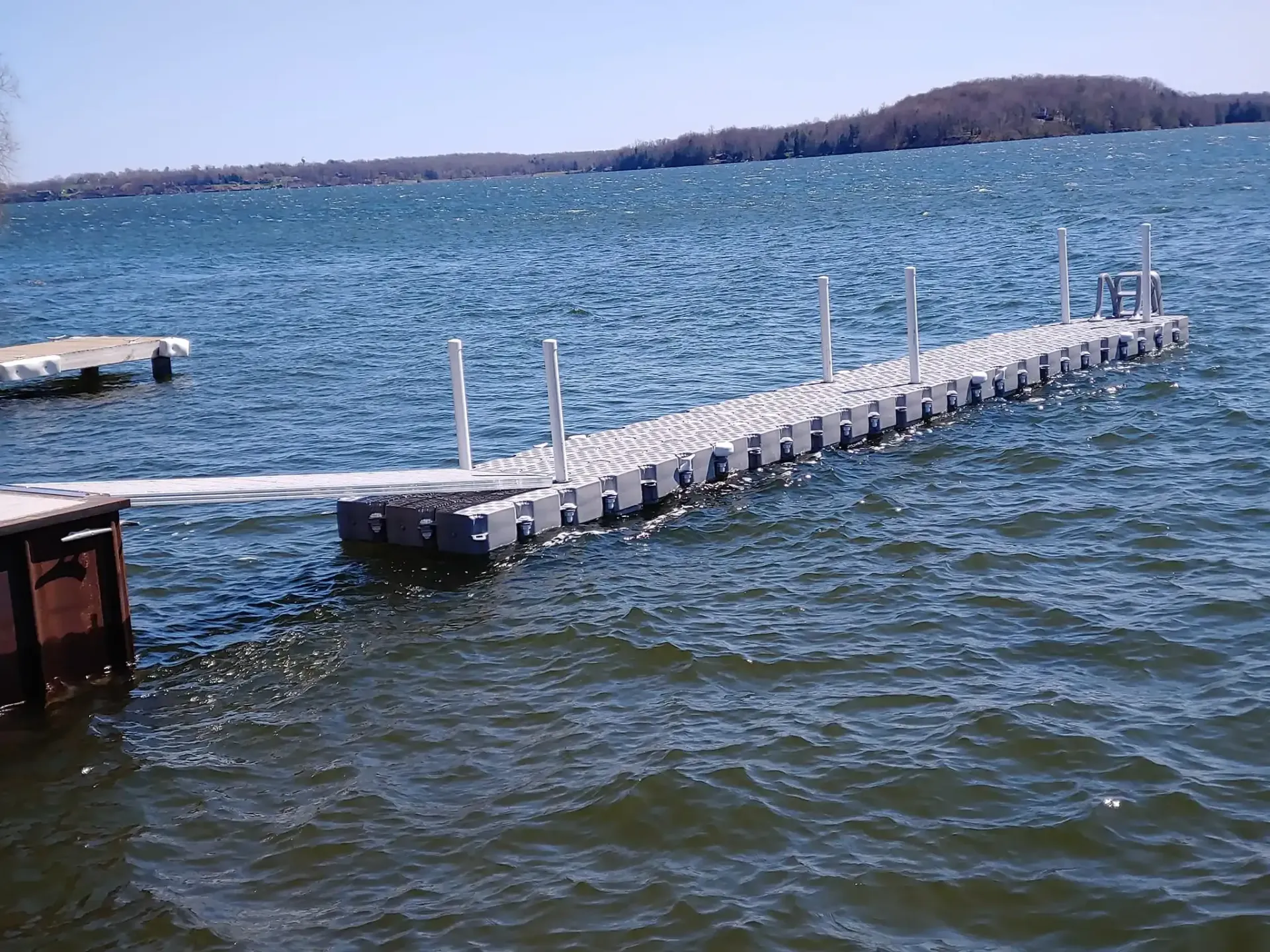 Floating dock on choppy blue water with a distant shoreline and small island under a clear sky