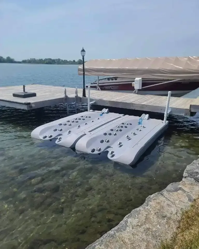 Four white floating paddleboards docked at a lakeside pier under a canopy.