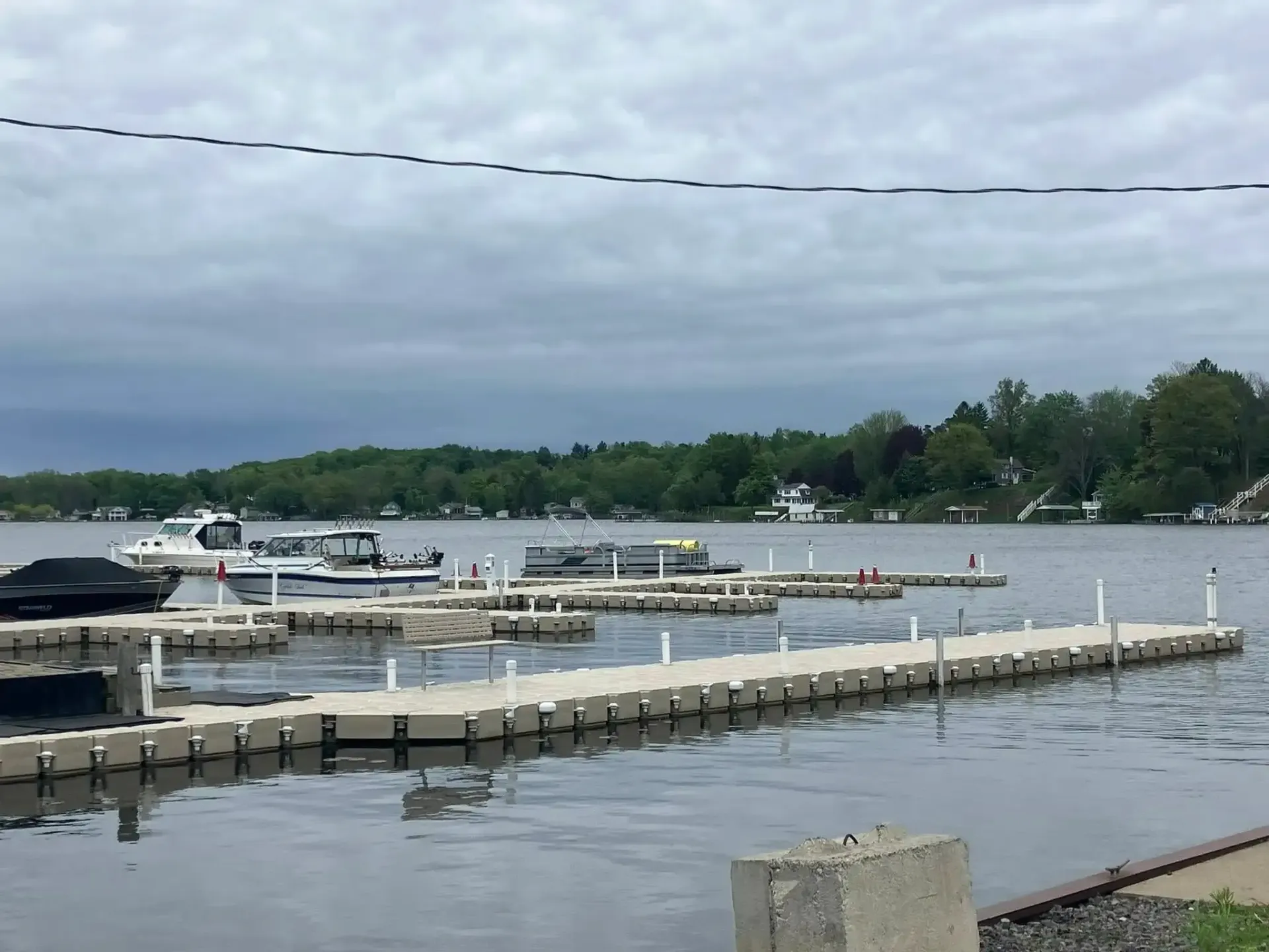 Marina with boats and docks on a cloudy waterfront, with trees lining the far shore