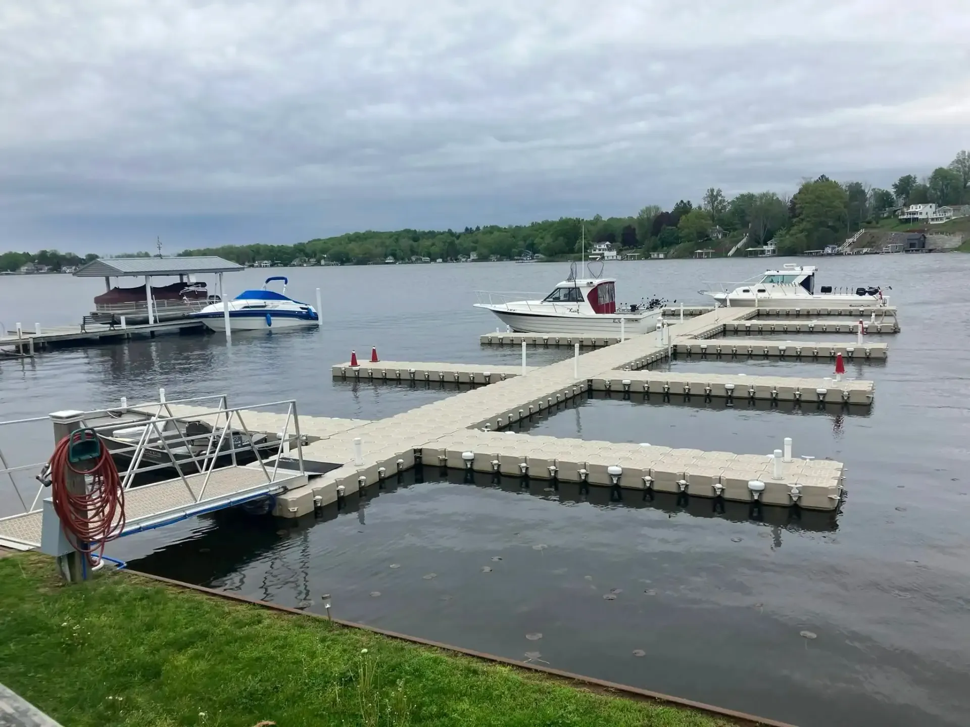 Floating dock with several boats on a cloudy lake, seen from a grassy shore