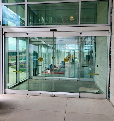 Automatic sliding glass doors at a modern building entrance with yellow caution decals on the glass.