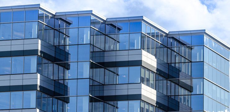 A modern office building with a glass facade reflecting the sky, seen from a low angle.