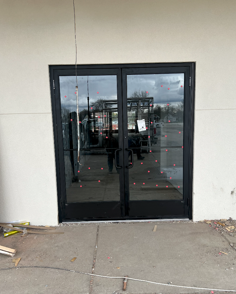 Black double glass doors with a metal frame installed in a light-colored exterior wall.