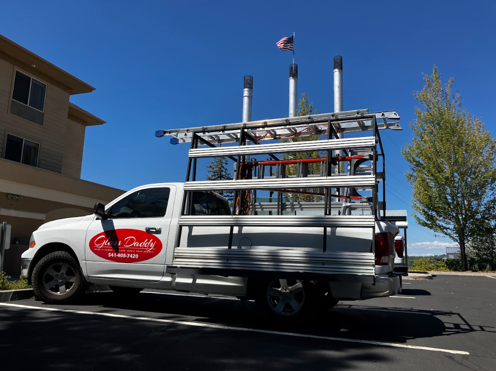 White service van with ladder rack and red logo parked on a sunny street under a clear blue sky