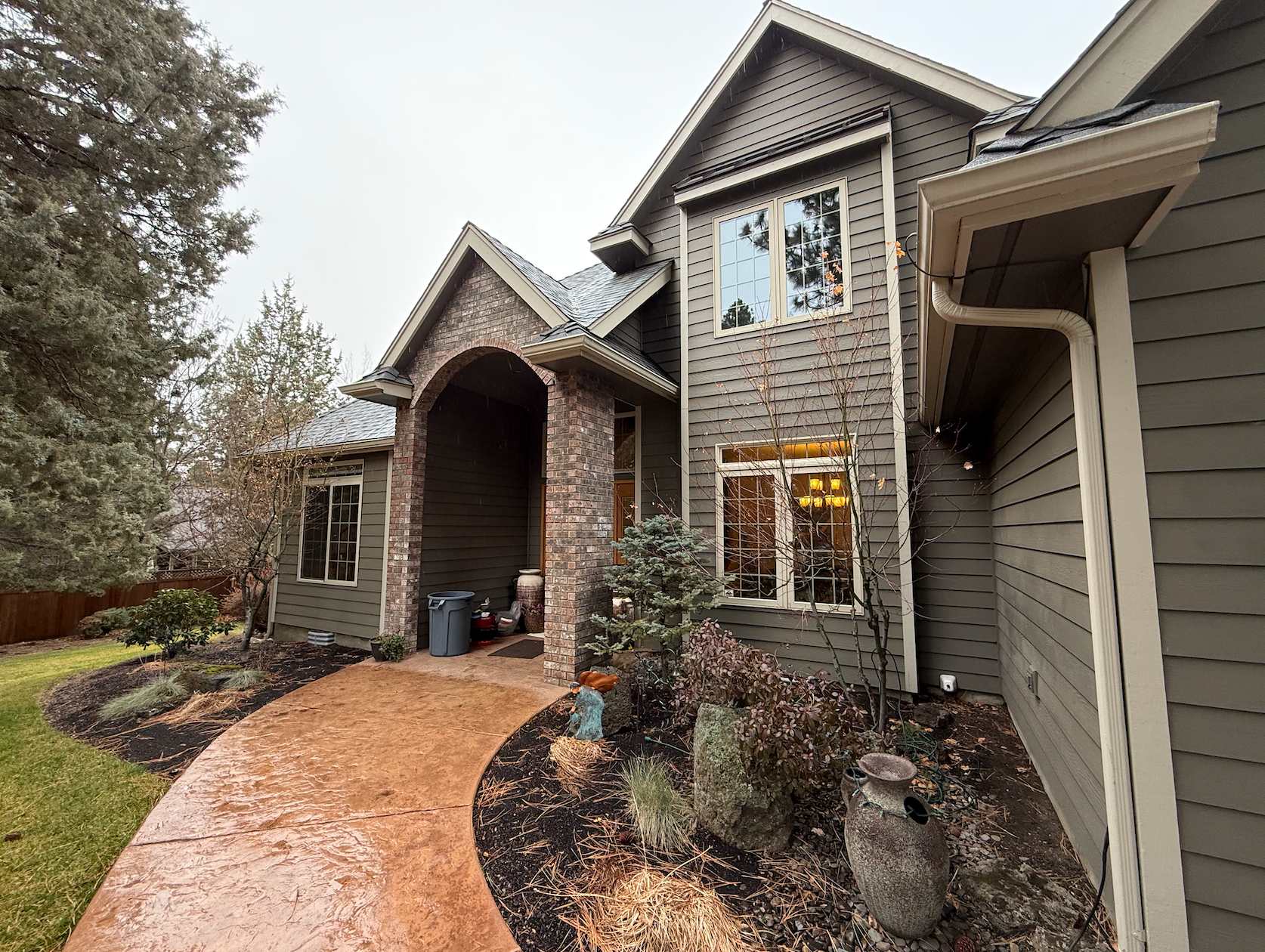 Brick house exterior with arched entry, stone façade, and a curving walkway lined with shrub