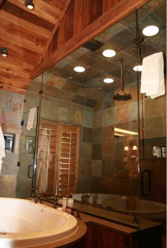 A spa-like bathroom with a white soaking tub, slate tile shower wall, glass enclosure, and wooden sloped ceiling.