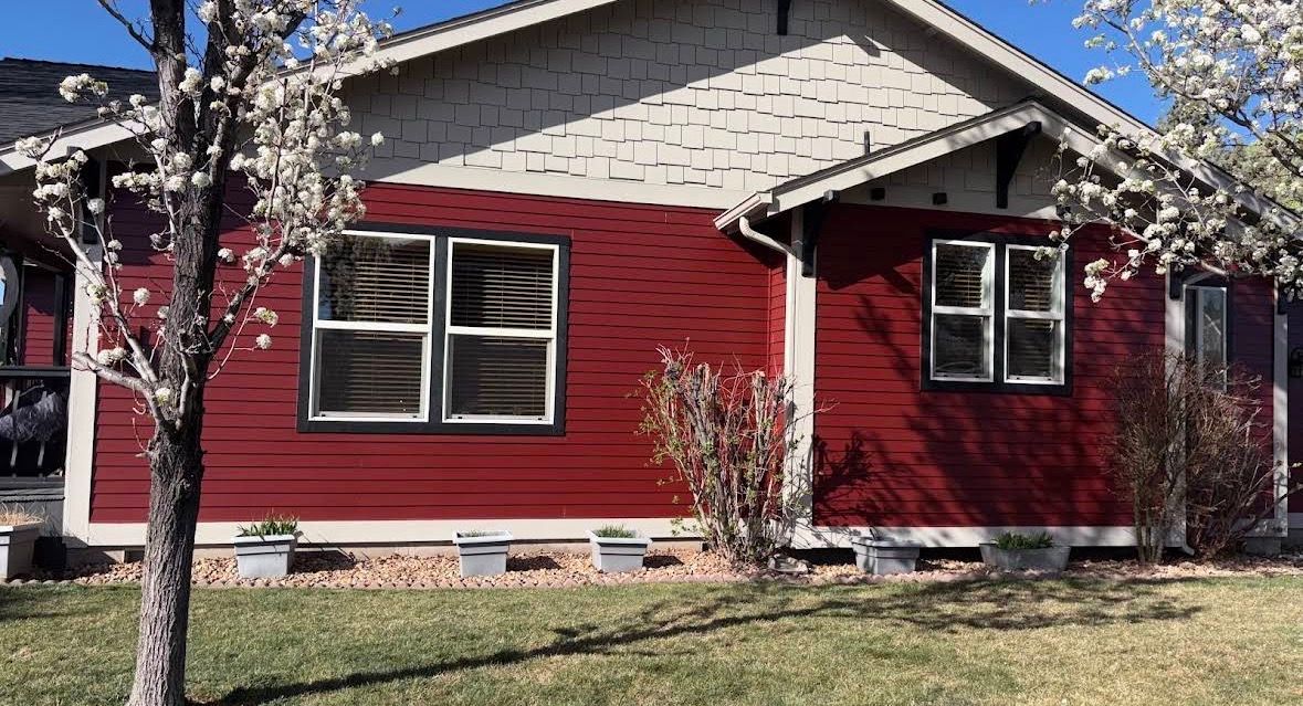 Red house with white trim and blooming trees in front yard