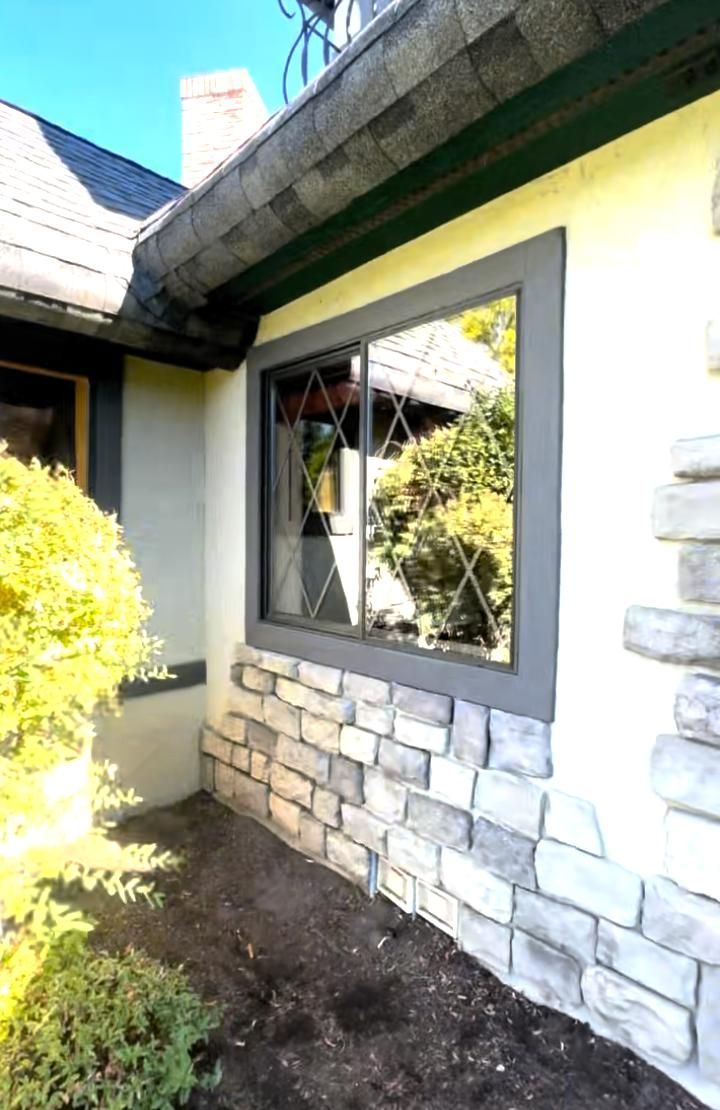 A rectangular window with a dark gray frame and diamond-patterned grid, set in a beige wall with a stone veneer base.