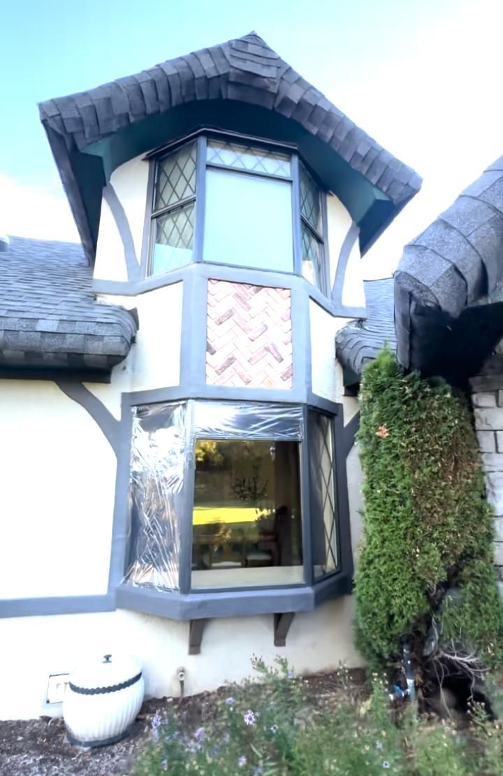 A Tudor-style home exterior featuring a turret with a top-floor window, a lower bay window, and gray roof shingles.