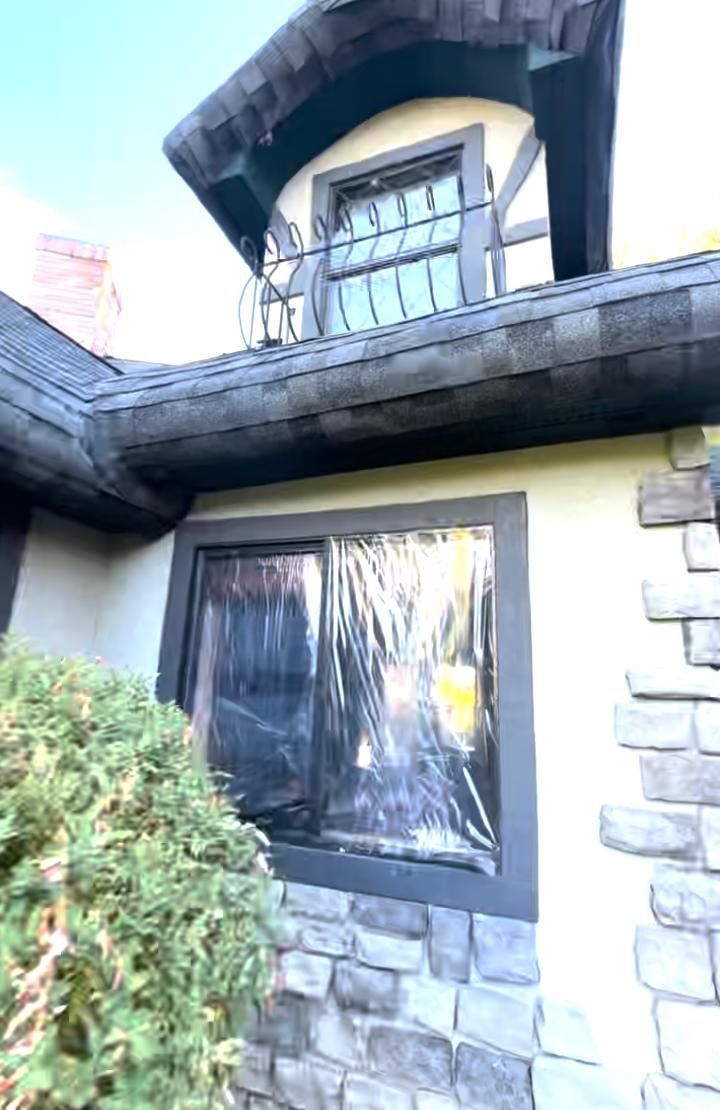 A stucco and stone-facade house exterior featuring a second-story dormer window with iron railing and a ground-floor window.