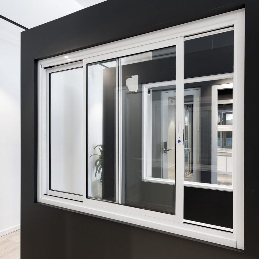 A three-panel white sliding window frame set against a black wall, showing a reflection of a room interior.