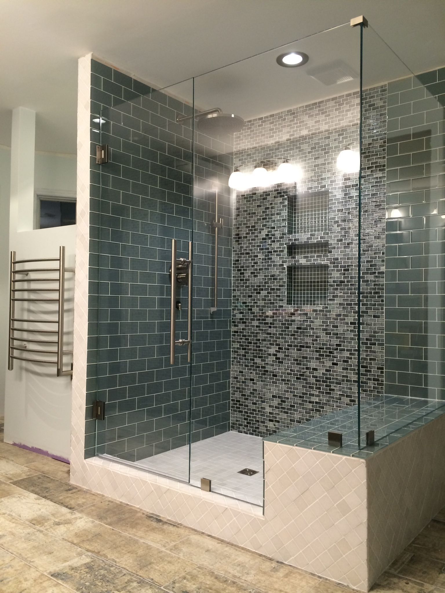 A modern shower enclosure with a geometric-patterned glass door, a tiled black-and-white wall, and a metal towel warmer.
