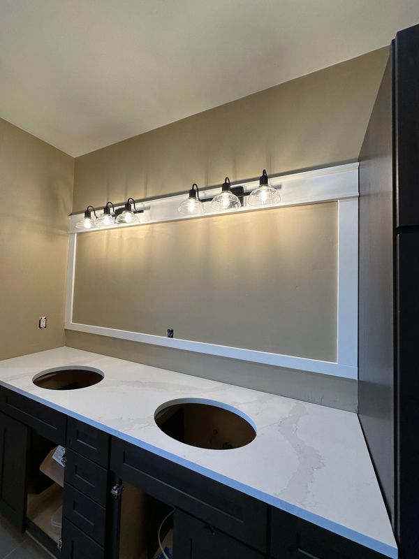 A bathroom vanity with dark cabinets, a white marble-patterned countertop with two cutouts, and a light fixture above.