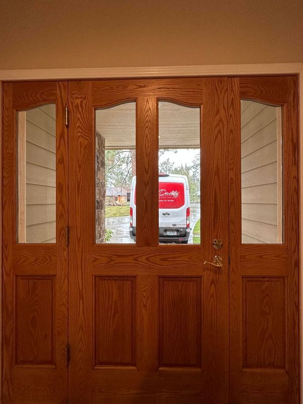 A wooden front door with four glass panels, looking out onto a residential street with a white van parked outside.