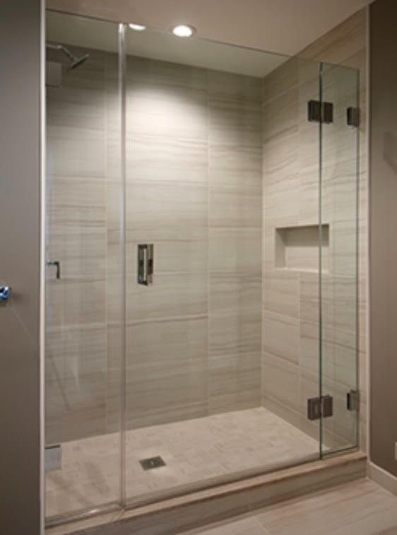 A walk-in shower with a glass door, neutral-toned tiled walls, and a small recessed shelf, set in a modern bathroom.