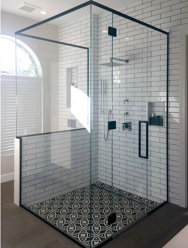 Modern walk-in shower with black-framed glass, white subway tile walls, and patterned black-and-white floor tiles.