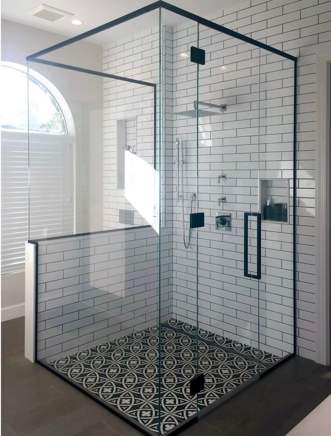 Modern glass shower enclosure with black framing, white subway tile walls, and patterned black and white floor tiles.