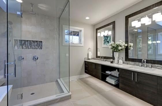 A modern bathroom featuring a glass-enclosed shower, a long vanity with dark wood cabinets, and two large wall mirrors.
