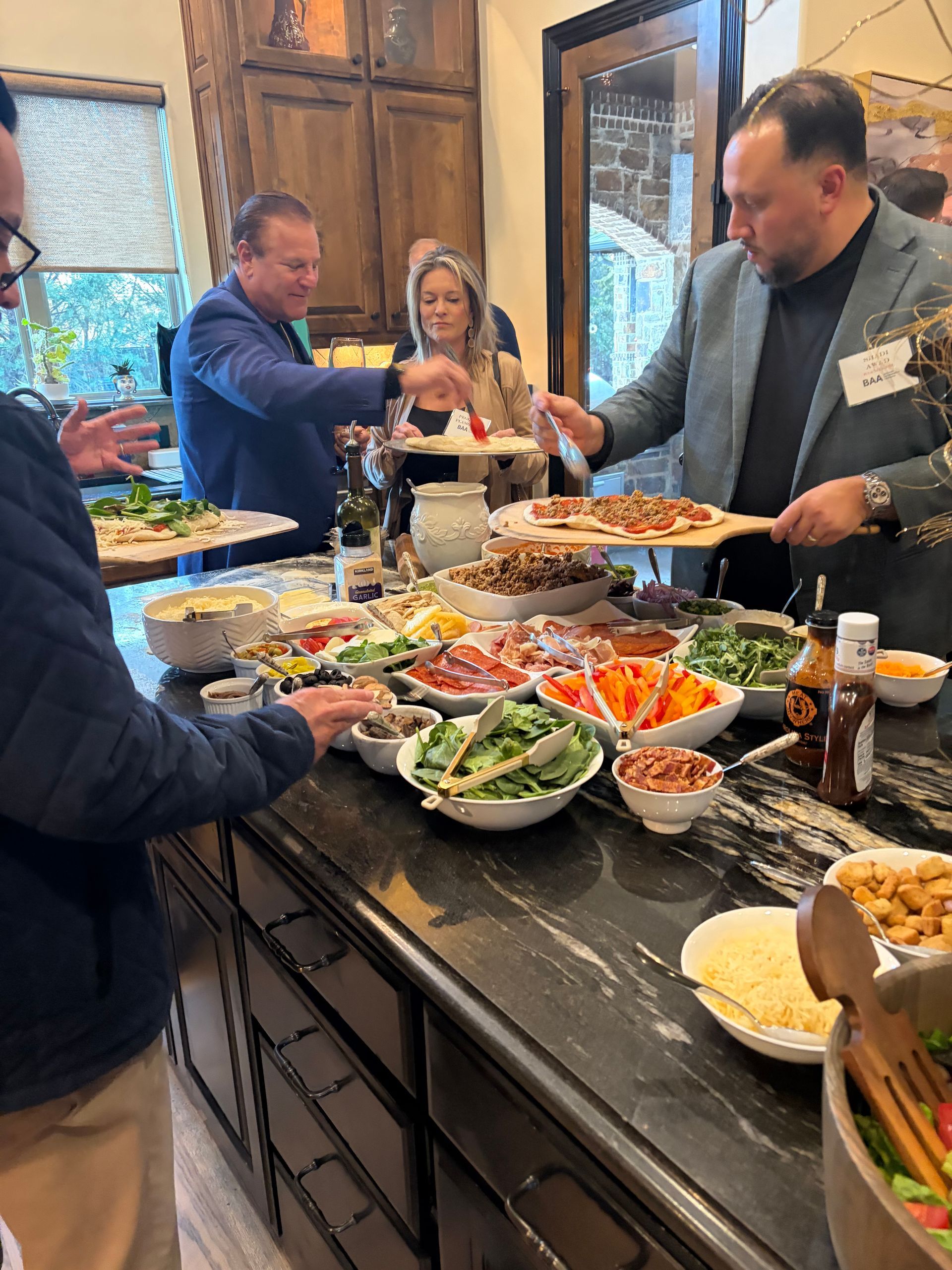 People serve themselves from a buffet of salads and appetizers arranged on a kitchen island during a social gathering.