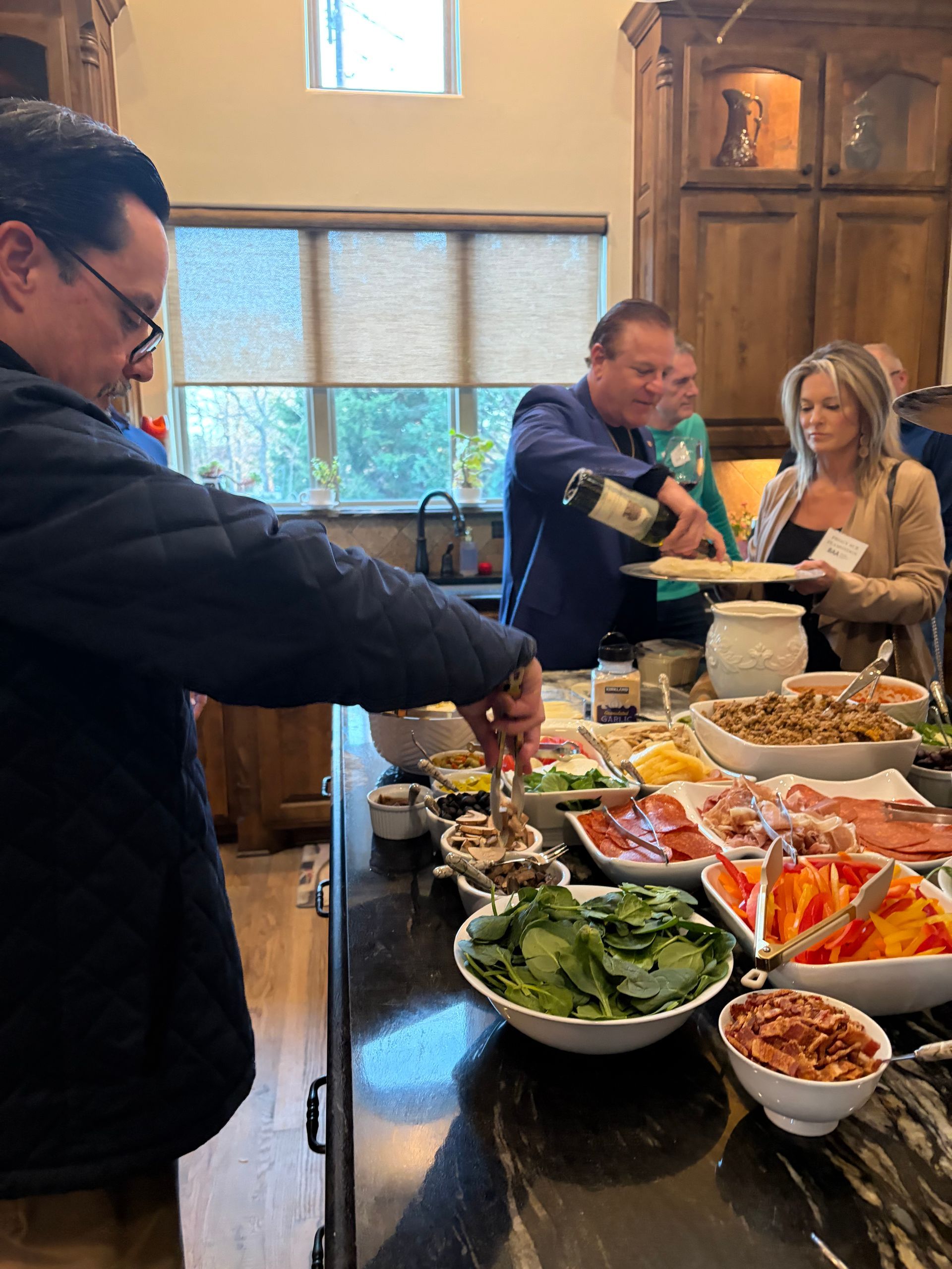 People gathered around a kitchen island preparing food and drinks at a social event.