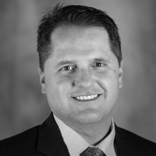 Headshot of a smiling person wearing a suit and tie against a blurred background.