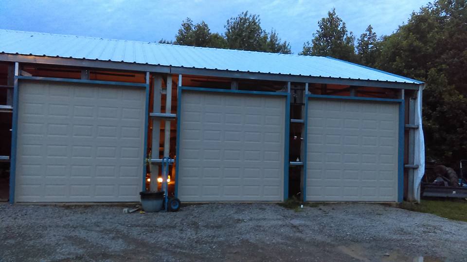 Three-bay garage with white doors, metal roof, and blue frames. Dusk setting.