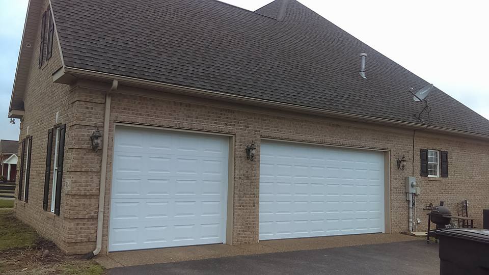 Two-car garage with white doors, on a brick house. Overcast sky.