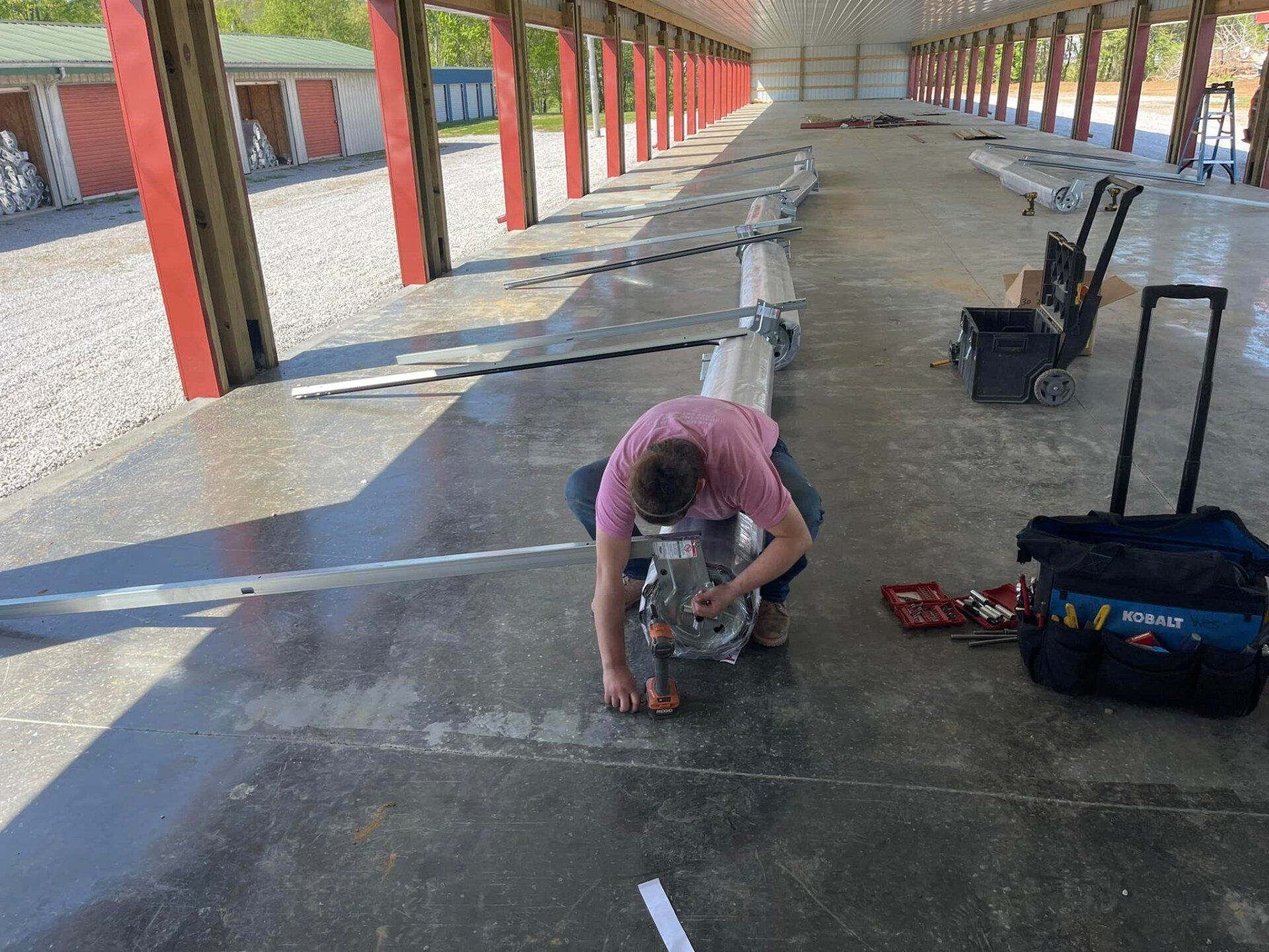 A person works on machinery inside a building. Tools and parts scattered nearby.
