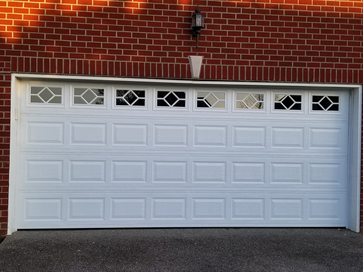 White garage door with geometric top windows against a red brick wall.
