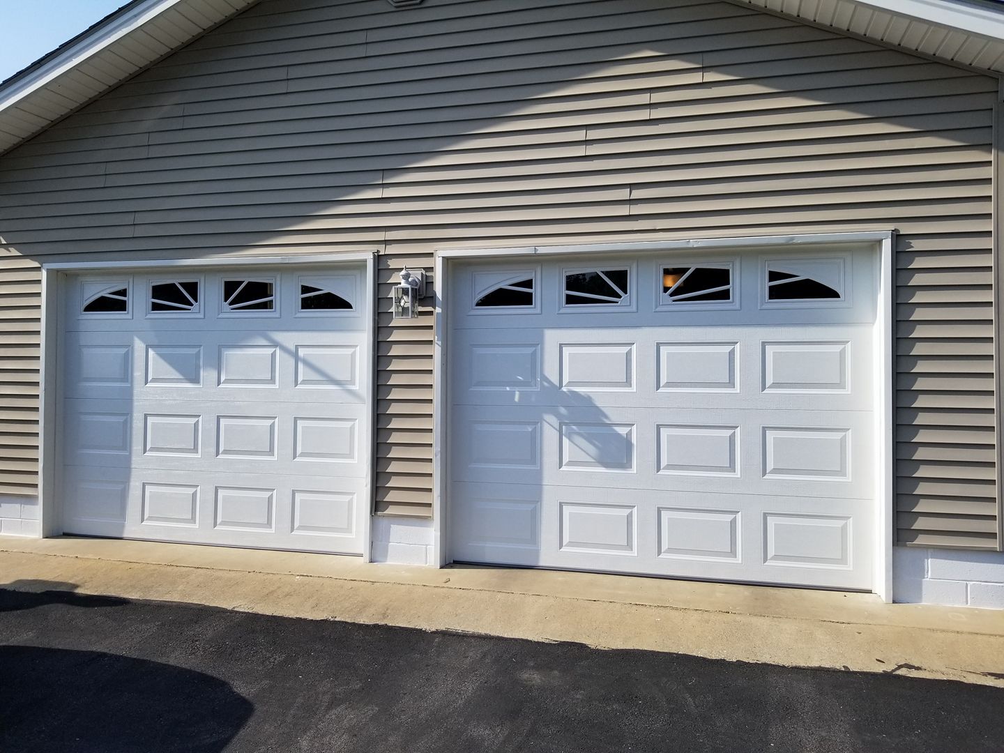 Two white garage doors on a light brown building with matching siding.
