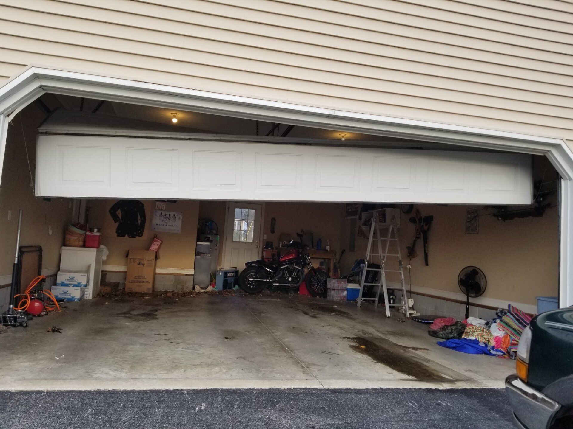 Garage door partially open, revealing cluttered interior, including a motorcycle and a ladder.
