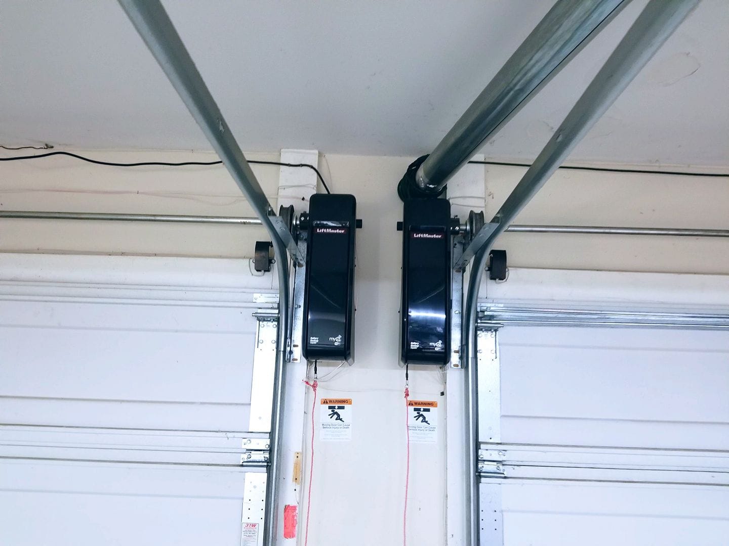 Two black garage door openers mounted above white garage doors.