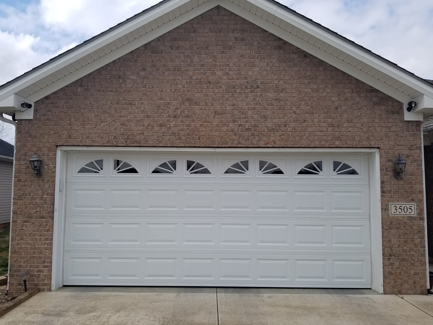 White garage door with arched window panes, brick exterior.