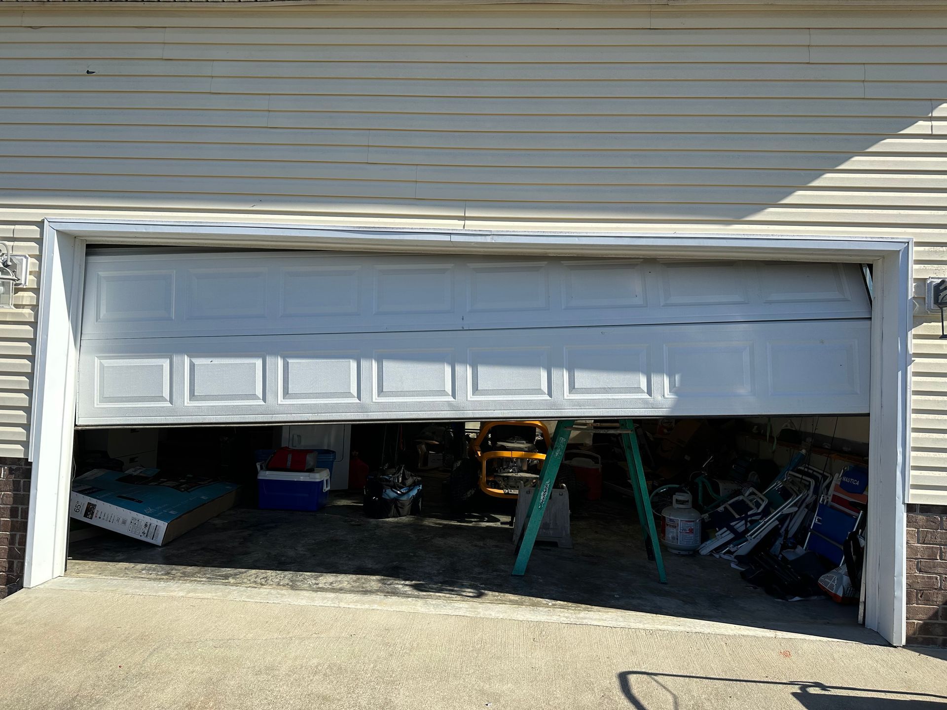 Garage door partially open, revealing a cluttered interior. White door, concrete driveway, siding above.