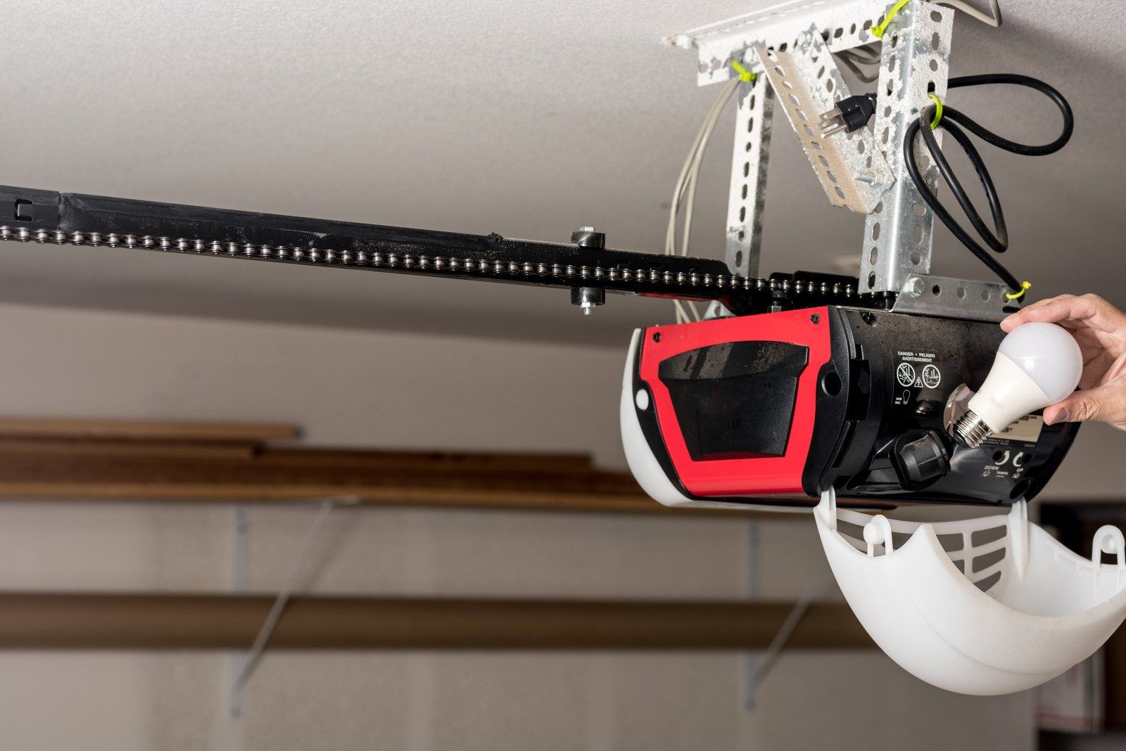 Person replacing a lightbulb in a garage door opener unit attached to a ceiling.