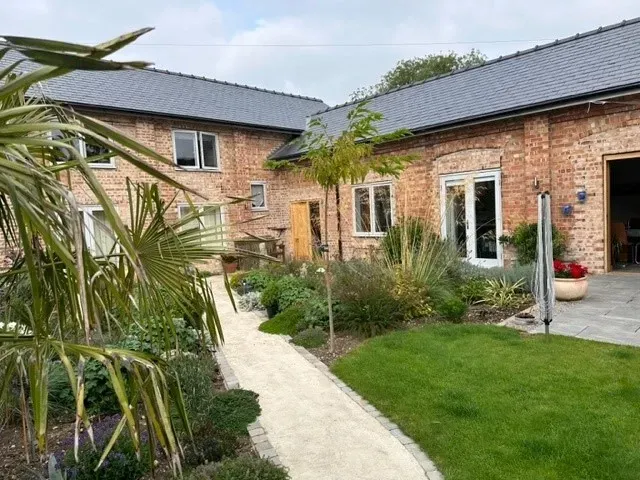 A brick house with a walkway leading to it and a lush green yard.